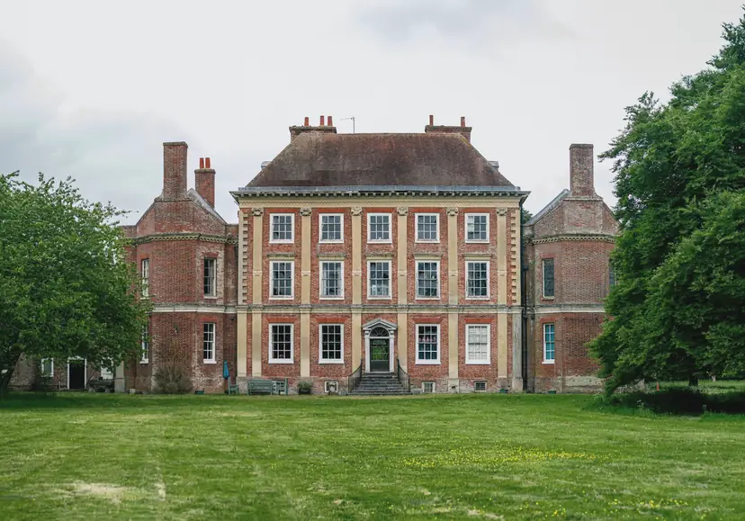 A brick manor house and lawn under a flat grey sky, as a typical listing photograph